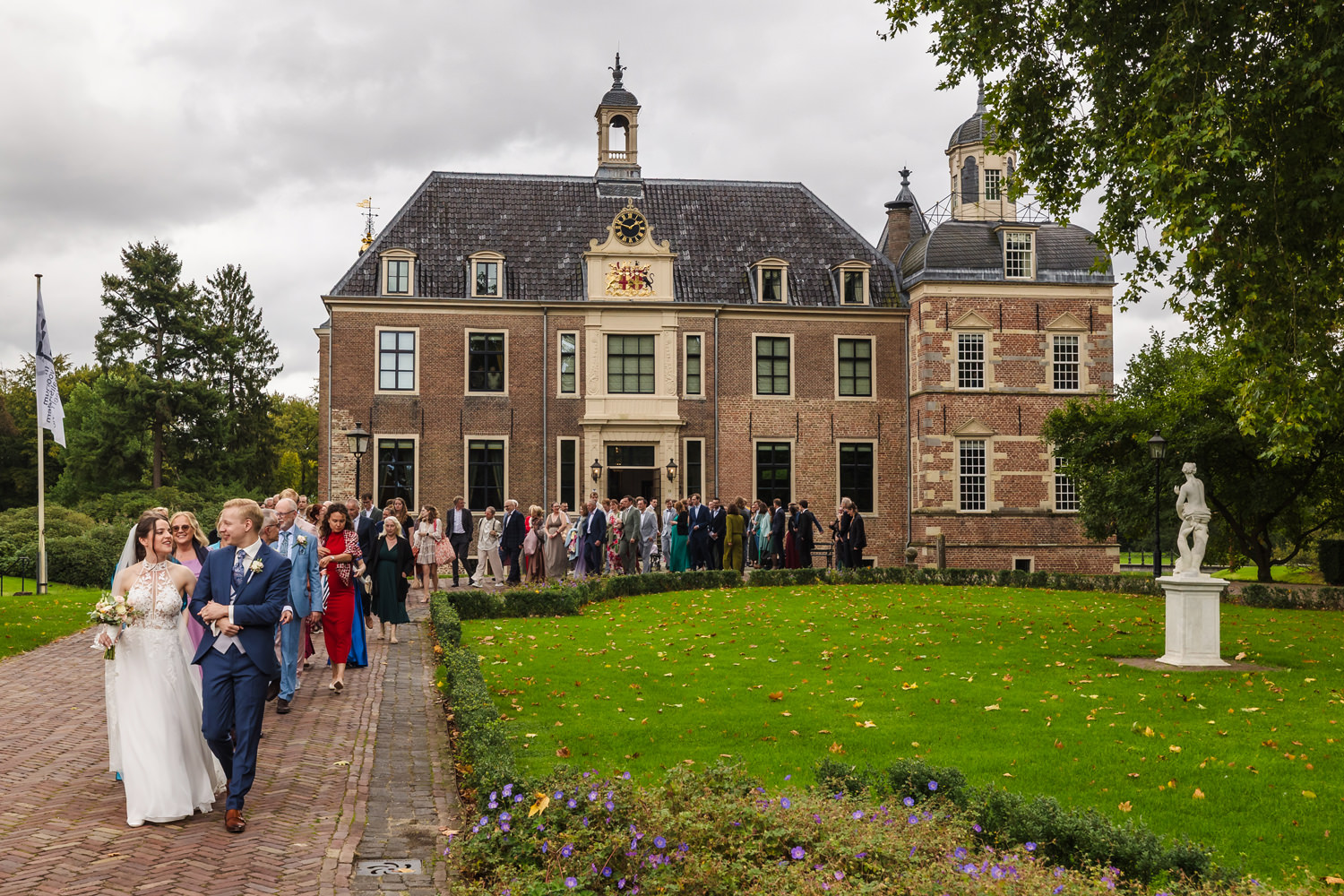 bruidspaar en gasten lopen voor trouwlocatie kasteel ruurlo langs