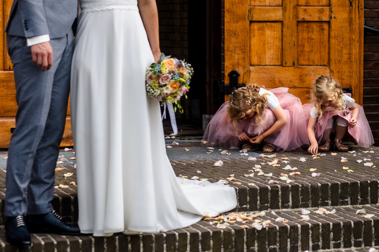 bruidsmeisjes rapen bloemblaadjes voor de kerk met bruidspaar op de voorgrond