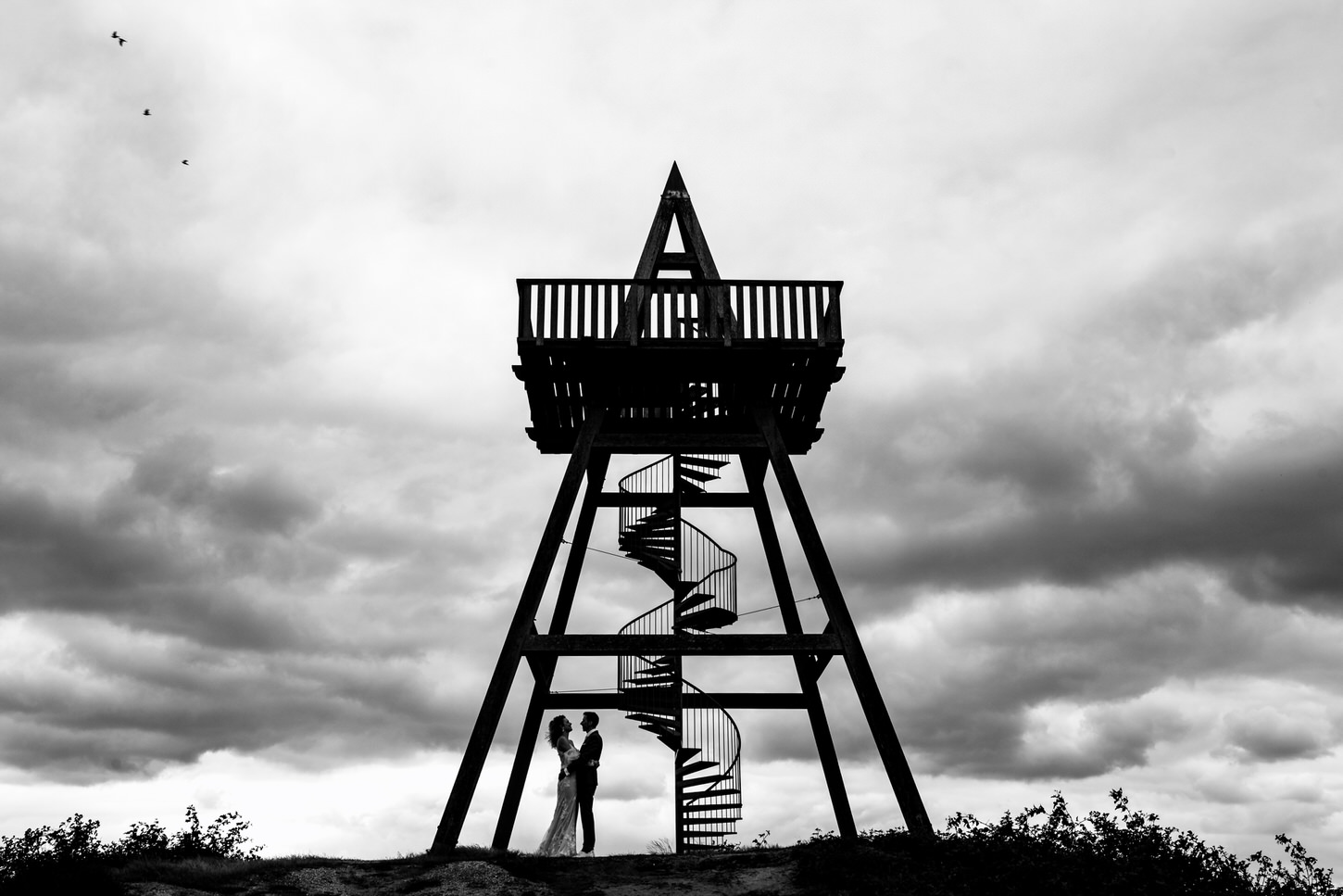 bruidspaar op uitkijktoren met donkere lucht en vogels