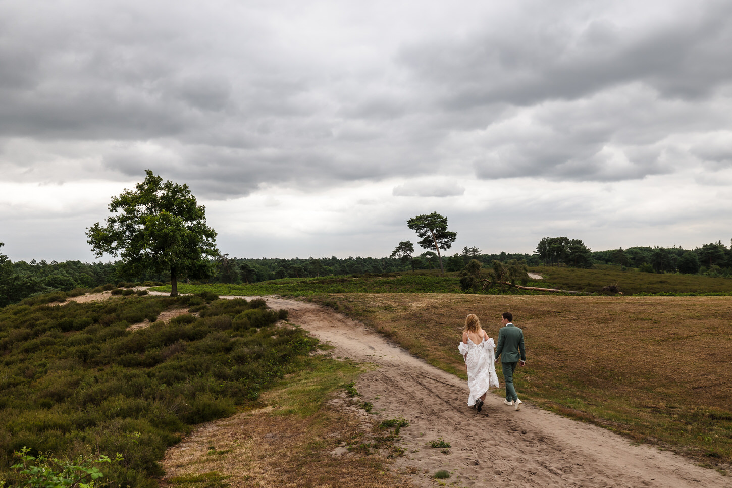 bruidspaar wandelt over de heide met donkere lucht op de achtergrond
