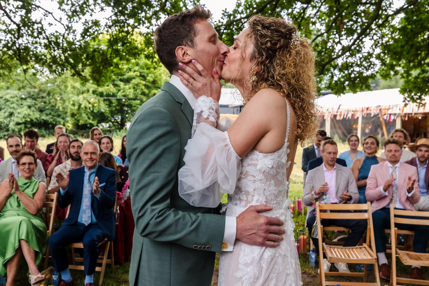 eerste kus van het bruidspaar met applaudisserende gasten op de achtergrond