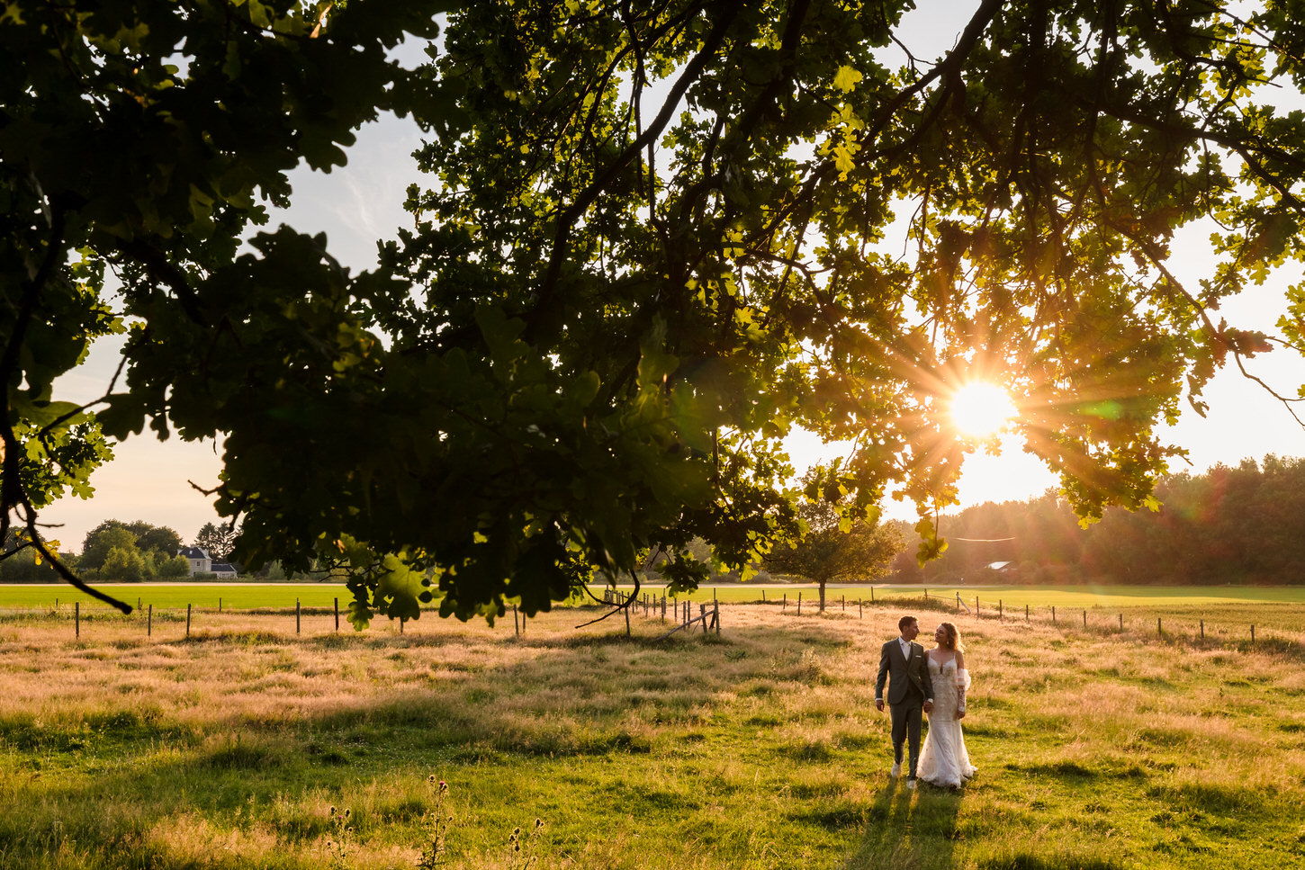bruidspaar wandelt door het gras met de avondzon op de achtergrond