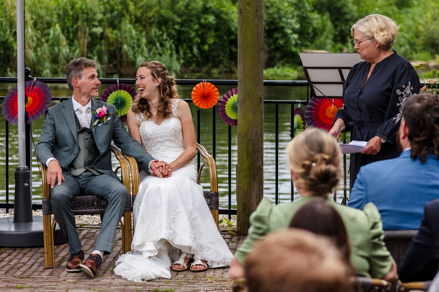 bruidspaar op een bankje tijdens de trouwceremonie bij de vief heringe, rechts staat de trouwambtenaar