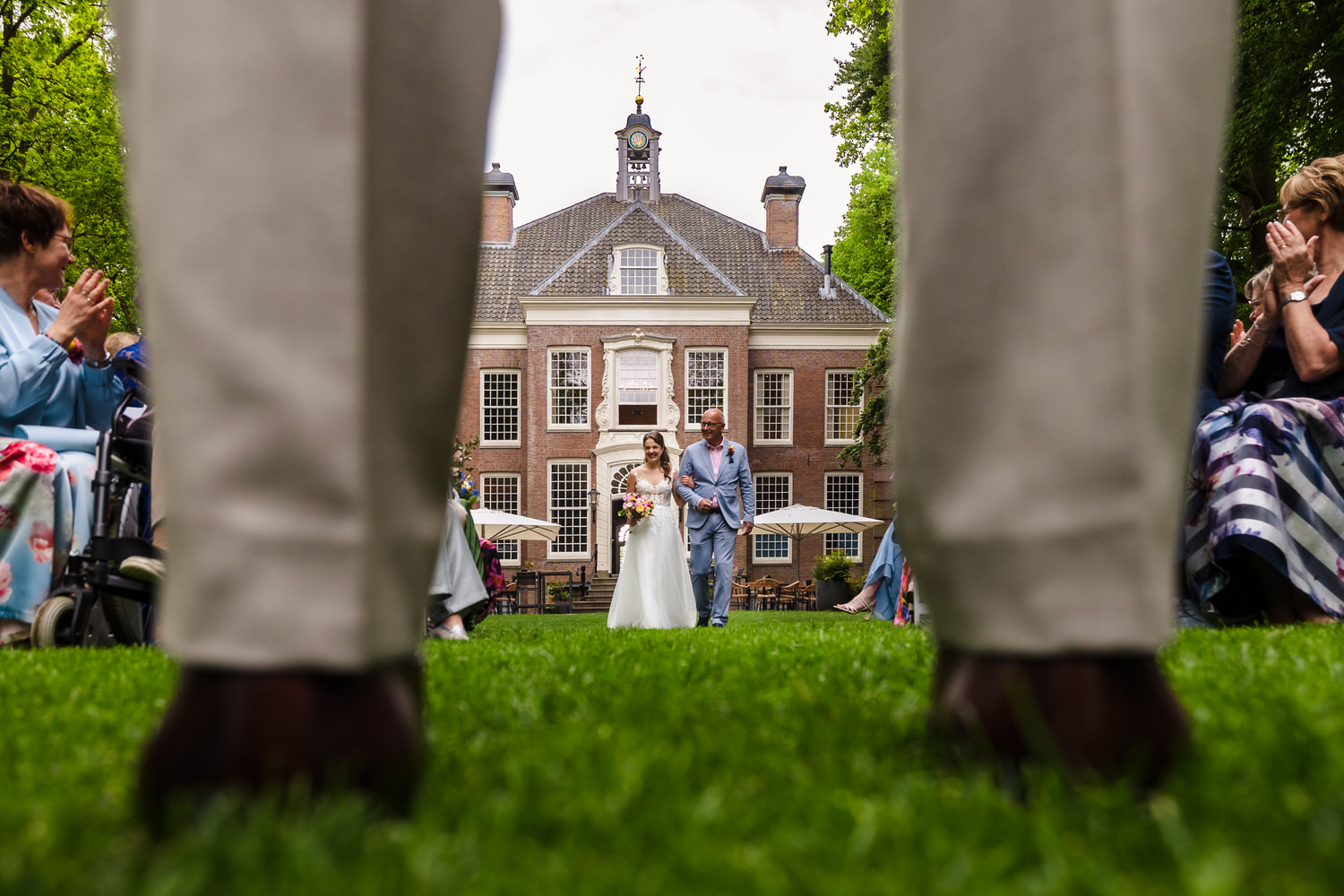 bruid loopt op met vader, gezien door de benen van de bruidegom