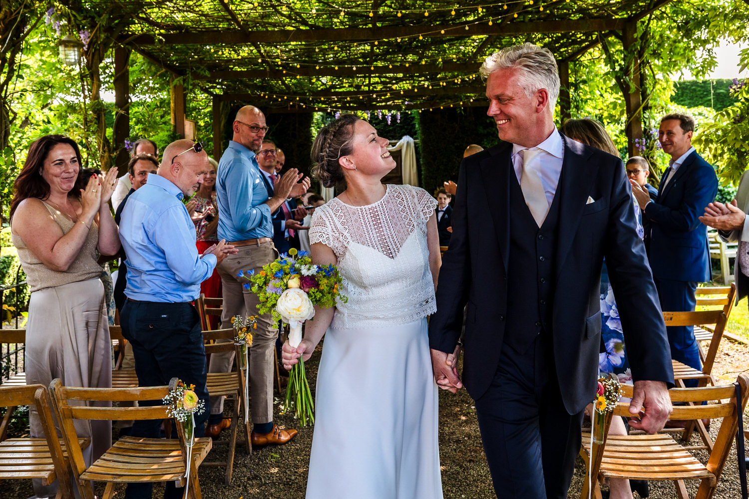 bruidspaar loopt na afloop van de ceremonie weg onder de pergola van het hoogh huys in winssen