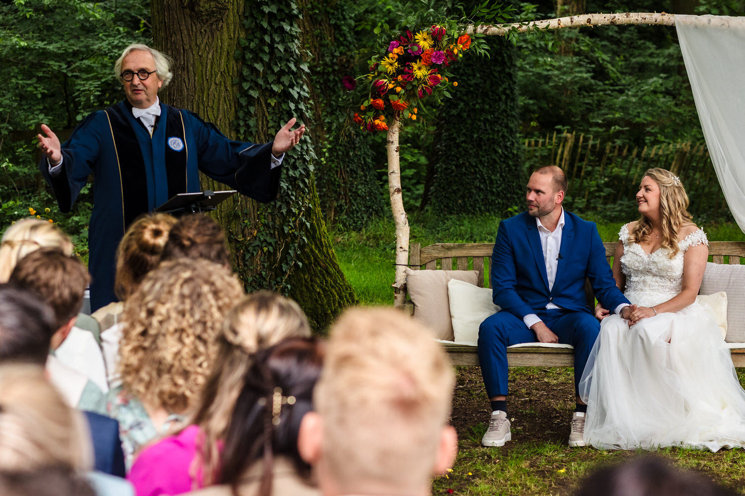 bruidspaar en gasten luisteren naar de ambtenaar tijdens een buitenceremonie bij landgoed brakksteyn in nijmegen