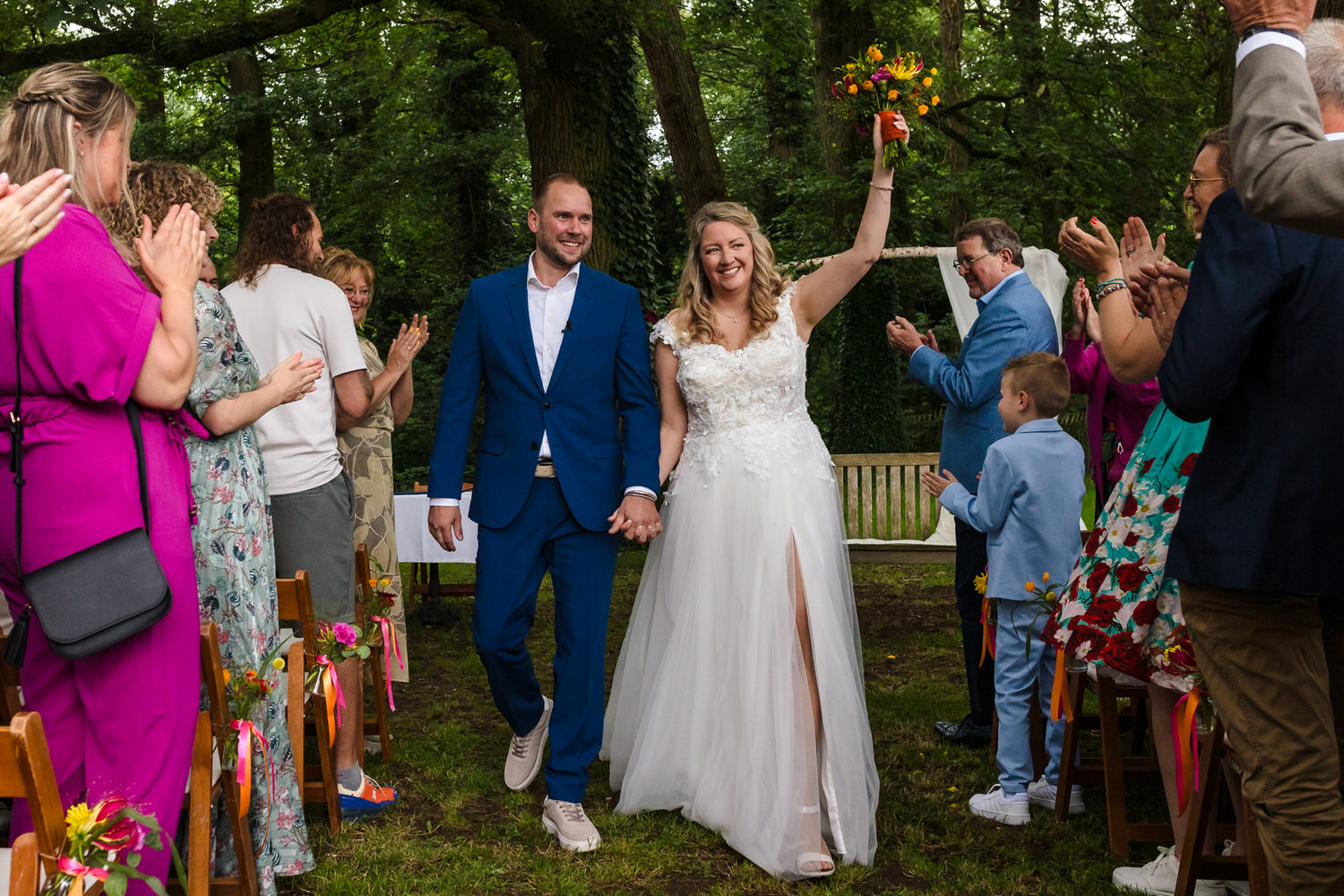 bruidspaar verlaat de ceremonielocatie, bruid steekt arm met boeket in de lucht