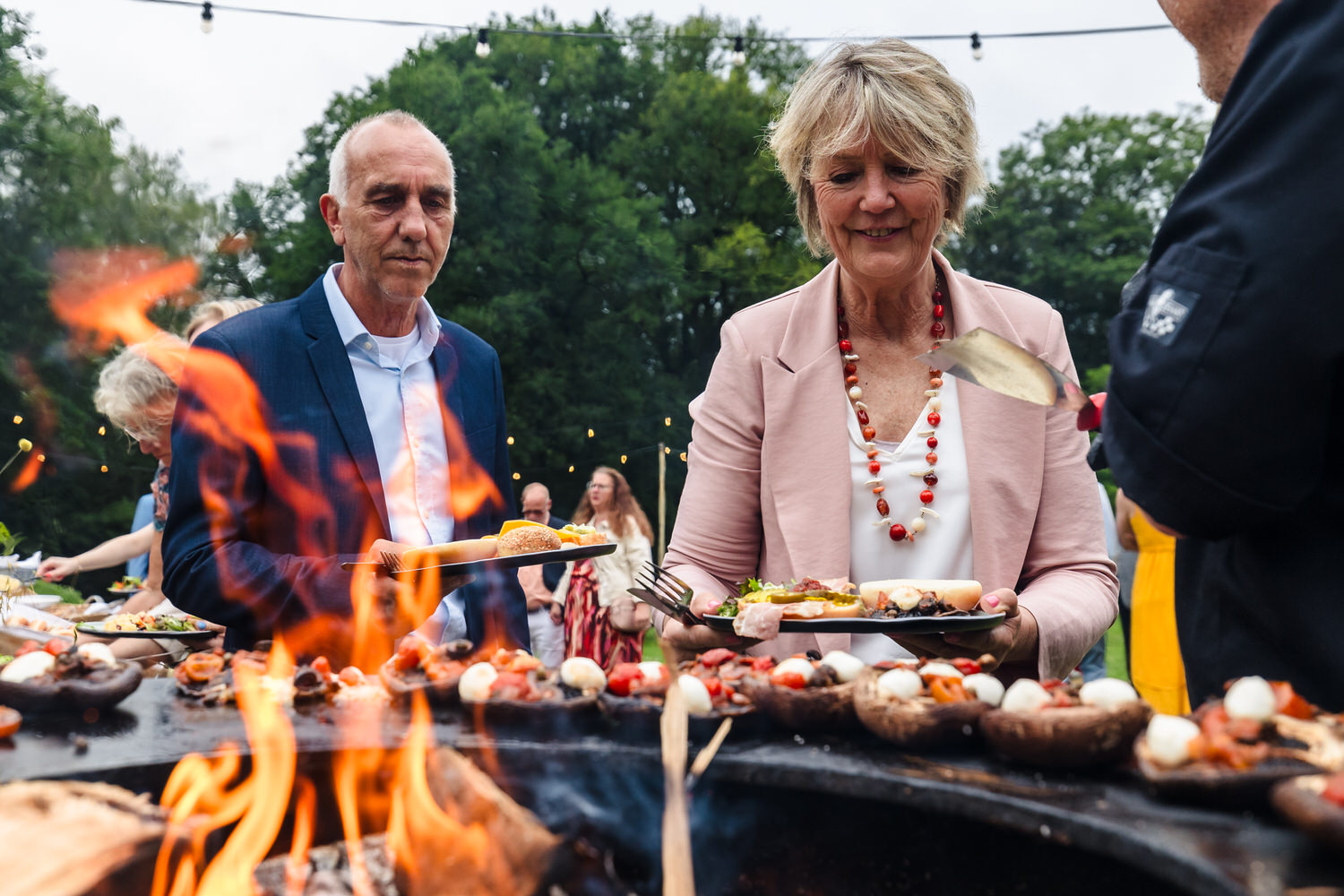 gasten scheppen eten op voor diner met het vuur van de barbecue op de voorgrond