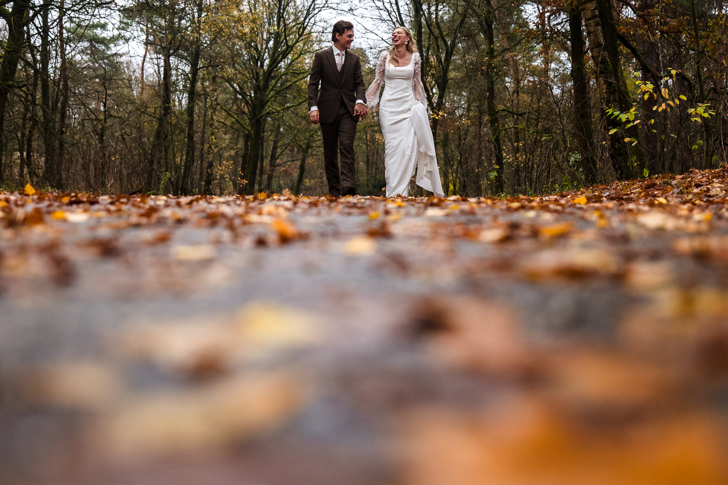bruidspaar wandelt over een weg vol herfstbladeren in het bos