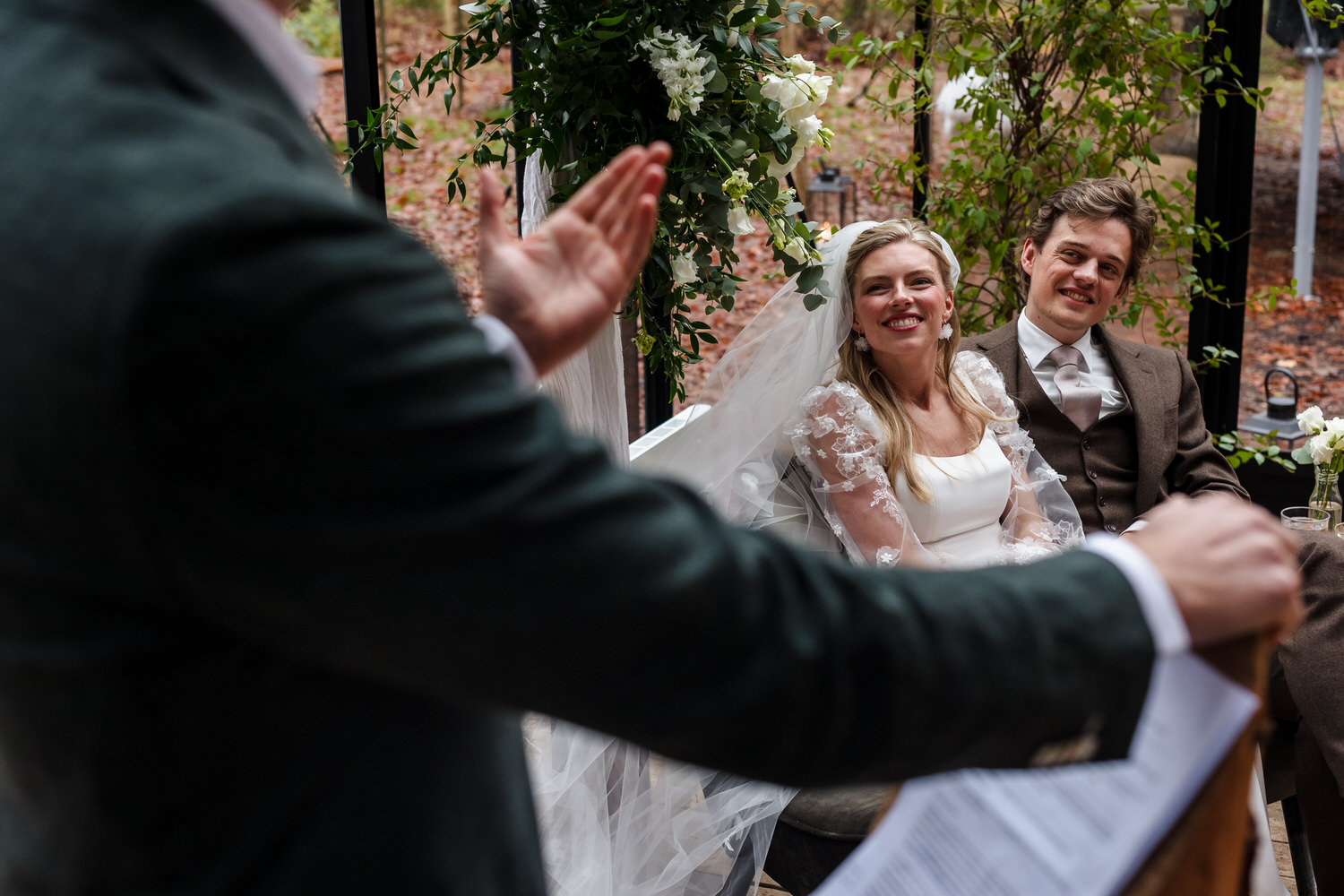 lachend bruidspaar kijkt naar de ambtenaar tijdens de ceremonie in de boskas in nijmegen